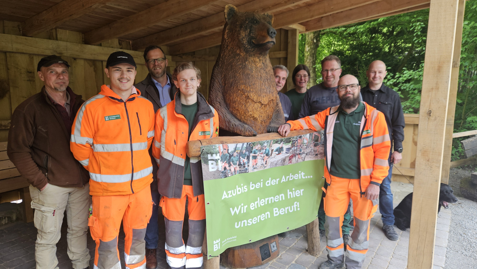 Das "Team Bärenhütte" um (vorne v.l.) Vincent Weber und Pascal Woltemate, Auszubildende des Fachbereichs Garten- und Landschaftsbau des Umweltbetriebs, sowie Ausbilder Malte Ihlenfeld. Kettensägenkünstler Sascha Eimertenbrink (rechts) hat die Bärenskulptur geschaffen. Foto: Stadt Bielefeld / Umweltbetrieb
