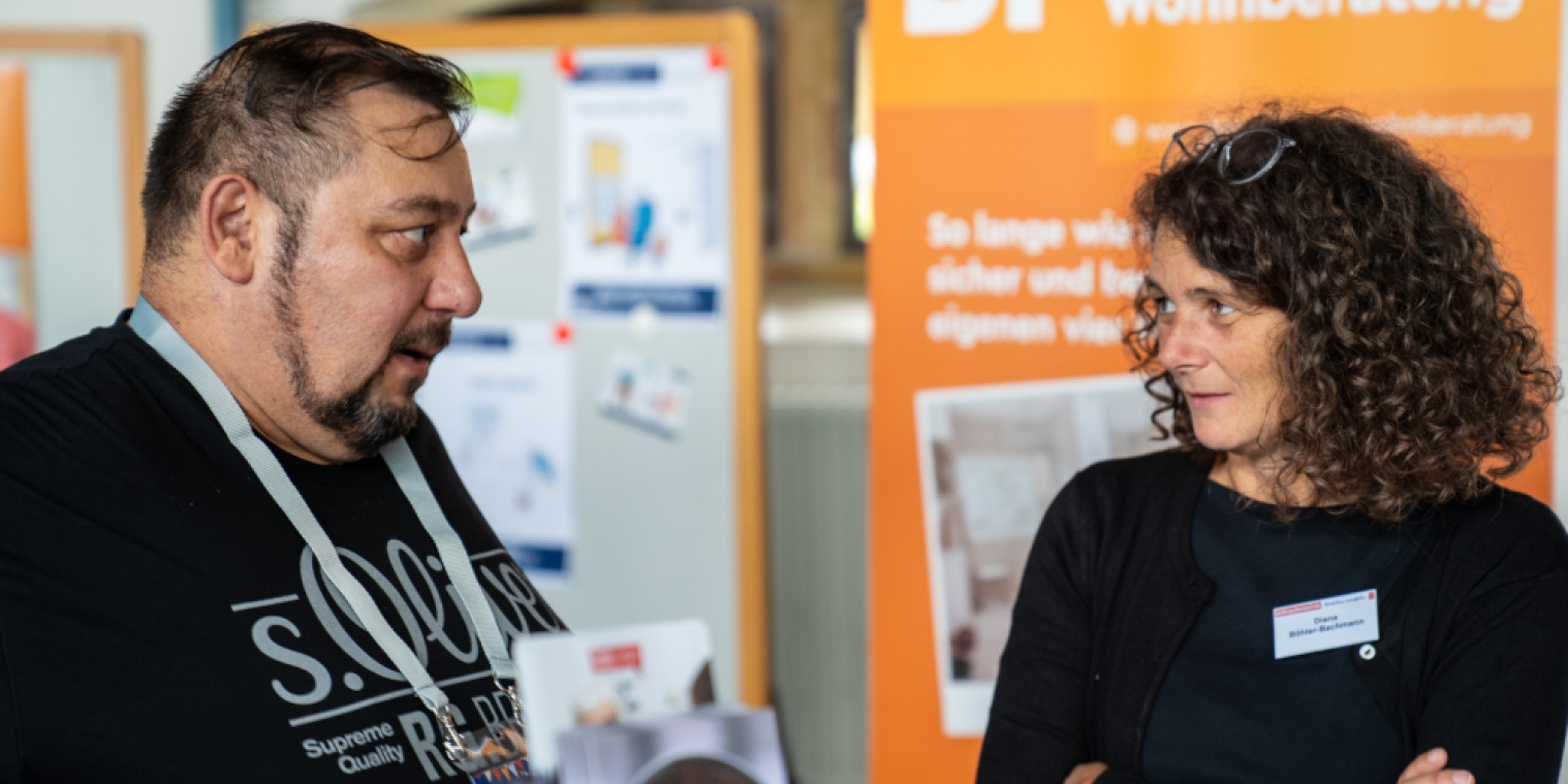 Zwei Menschen unterhalten sich vor einem Rollup der Bielefelder Wohnberatung.