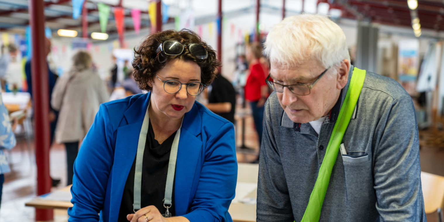 Eine Mitarbeiterin von CareTech OWL zeigt einem Mann den Infotisch. 