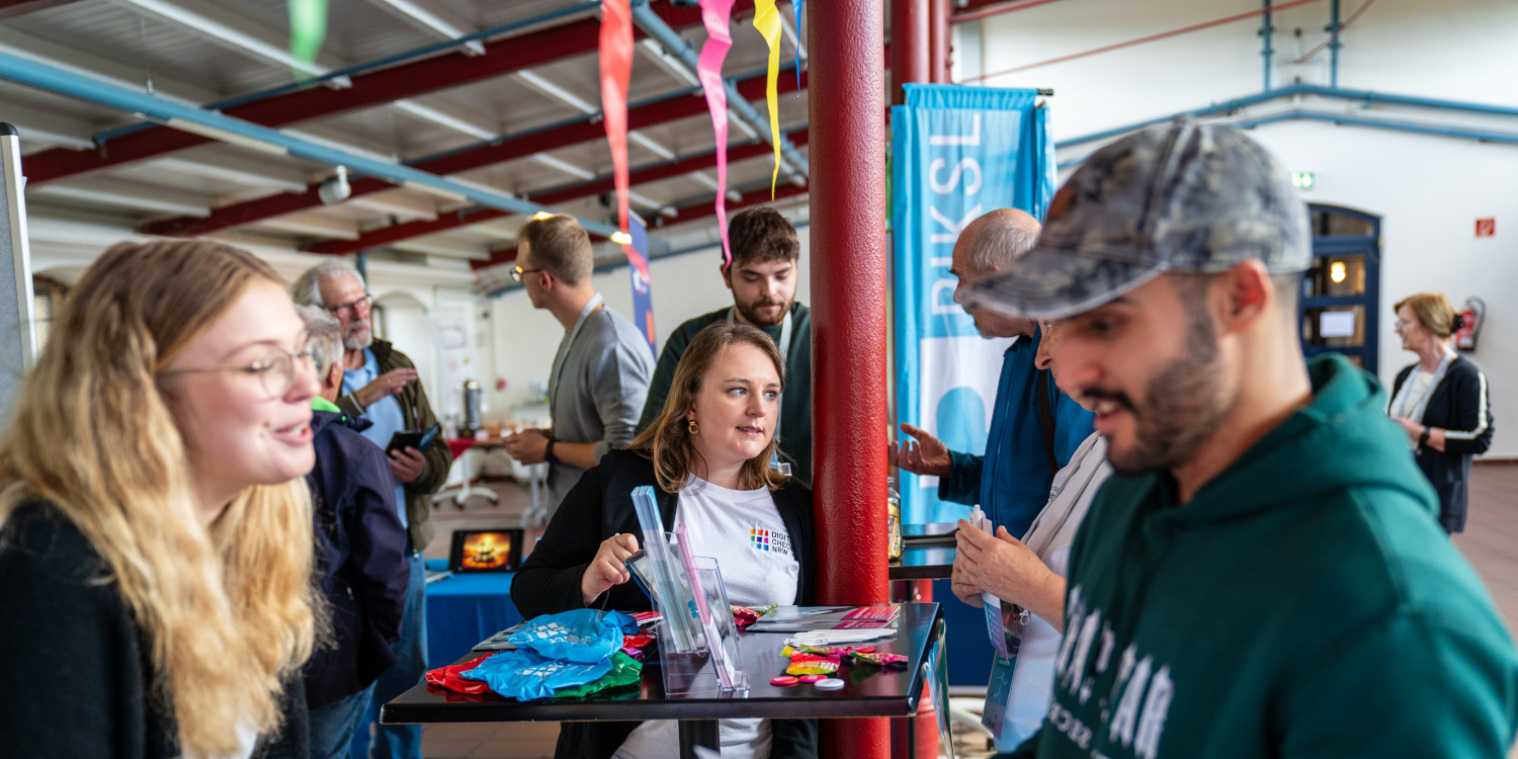 Eine Mitarbeiterin vom #DigitalcheckNRW unterhält sich mit einem Interessierten.