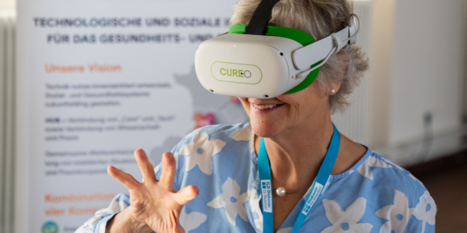 Eine ältere Frau probiert eine Virtual-Reality-Brille aus und lächelt dabei. 