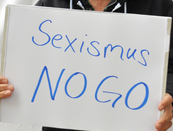 Hände halten Schild auf dem "Sexismus NOGO " steht.