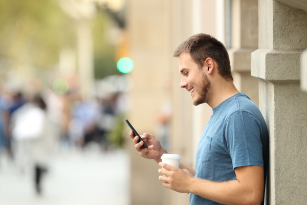 Ein junger Mann ist in der Stadt und schaut lächelnd auf sein Handy.