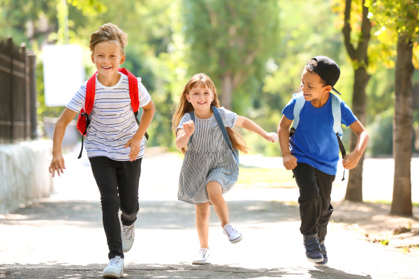 Drei Kinder laufen fröhlich ihren sicheren Schulweg entlang.
