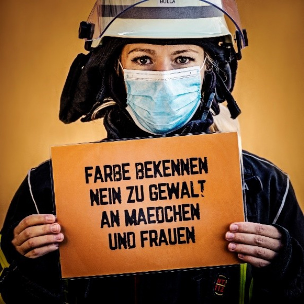 Feuerwehrfrau hält Plakat mit Statement zu "Nein zu Gewalt an Frauen" hoch.