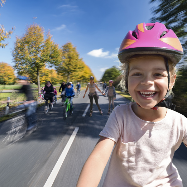 Ein fröhlich lachendes Kind auf dem Fahrrad, im Hintergrund weitere Radfahrende