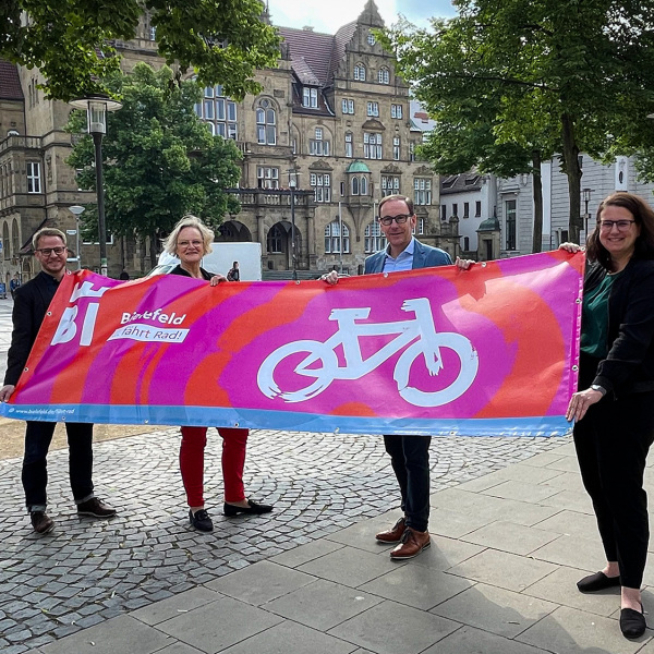 Vertreter*innen der Stadt Bielefeld halten ein Banner im neuen Design der Kampagne "Bielefeld fährt Rad"