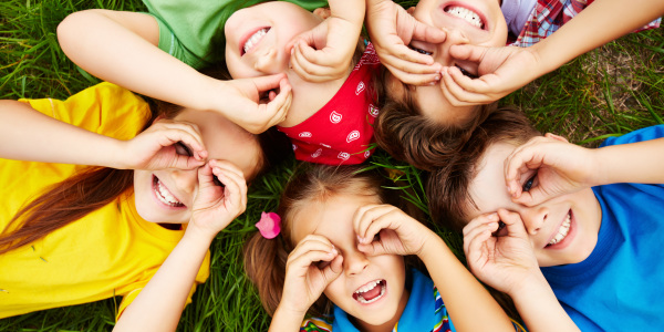 Mehrere Kinder liegen auf einer Wiese auf dem Rücken und formen mit den Händen eine Brille.