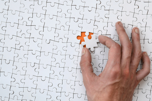 Die Textur eines weißen Puzzles im zusammengesetzten Zustand mit einem fehlenden Element, das die männliche Hand einsetzt.