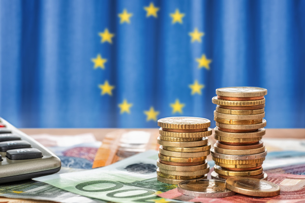Geldmünzen und Euro-Scheine vor einer EU-Flagge