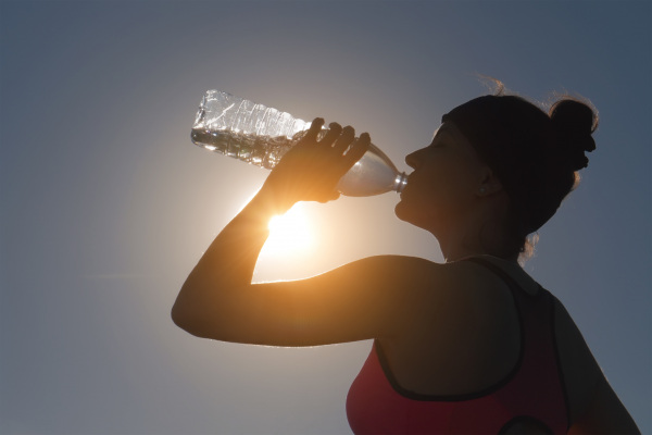 Eine Frau trinkt Wasser aus einer Flasche, die Sonne scheint von oben.