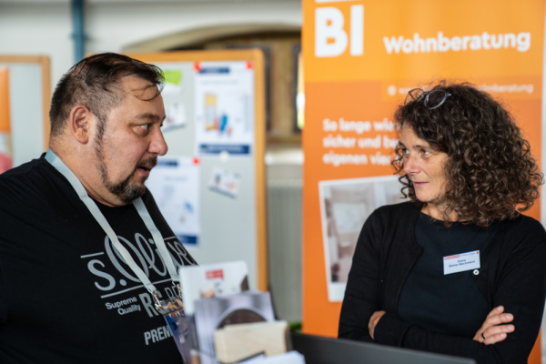 Zwei Menschen unterhalten sich vor einem Rollup der Bielefelder Wohnberatung.