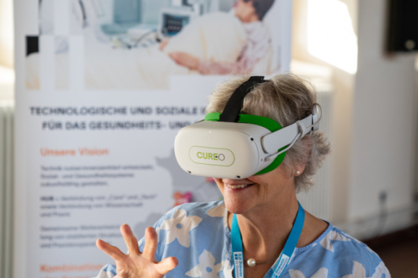 Eine ältere Frau probiert eine Virtual-Reality-Brille aus und lächelt dabei. 