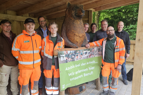Das "Team Bärenhütte" um (vorne v.l.) die Auszubildenden Vincent Weber und Pascal Woltemate sowie Ausbilder Malte Ihlenfeld vom Umweltbetrieb der Stadt Bielefeld. Kettensägenkünstler Sascha Eimertenbrink (rechts) hat die Bärenskulptur geschaffen. Foto: Stadt Bielefeld / Umweltbetrieb 