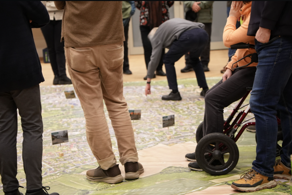 Das Bild zeigt die Teilnehmenden, die Maßnahmen-Vorschläge auf einem riesigen Stadtteil-Plan stehend mit den Planern diskutieren. Foto: Stadt Bielefeld