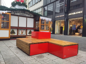 Die neuen Sitzbänke sind in rot gestrichen Die Sitzfläche ist aus hellem Holz gestaltet In der Mitte ist ein erhöhter Blumenkübel platziert